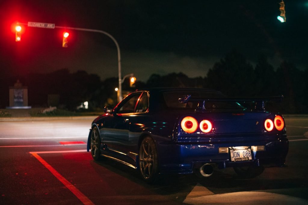 Blue Nissan Skyline GT-R at a city street intersection at night under red lights.