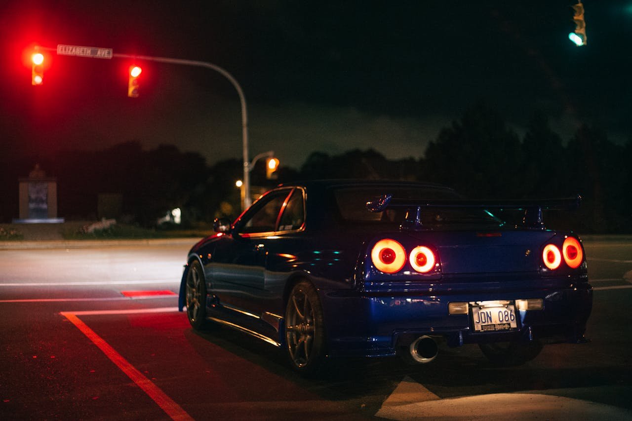 Blue Nissan Skyline GT-R at a city street intersection at night under red lights.